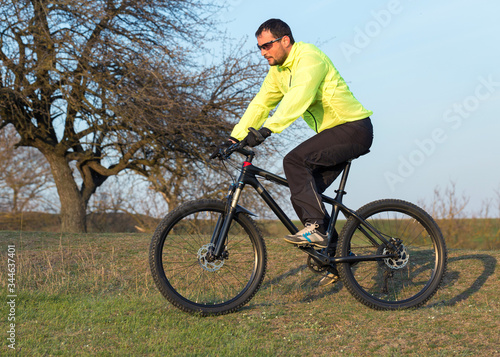 Fototapeta Naklejka Na Ścianę i Meble -  Cyclist in pants and green jacket on a modern carbon hardtail bike with an air suspension fork. The guy on the top of the hill rides a bike.