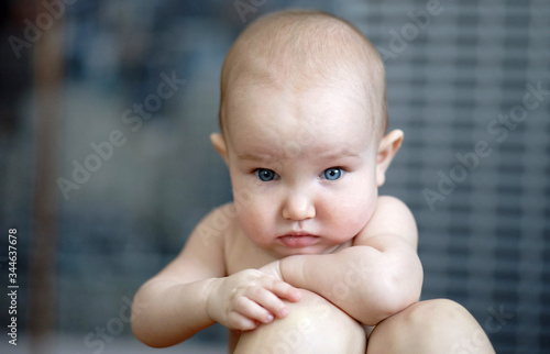 Portrait of little thoughtful baby with big blue eyes. Cute child with short hair, without shirt. Grey background