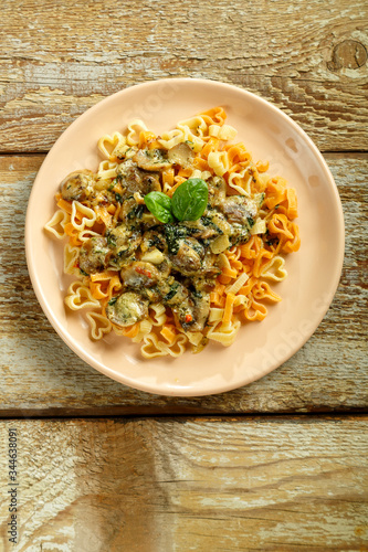 Plate of pasta with mushrooms in a creamy sauce with spinach on a wooden table.
