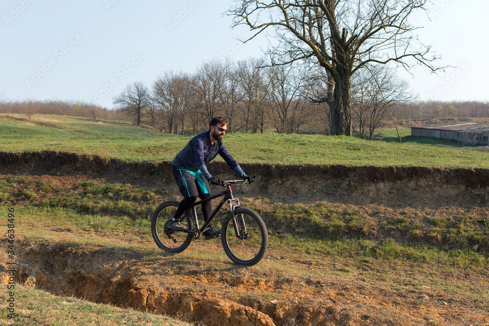 Cyclist in shorts and jersey on a modern carbon hardtail bike with an air suspension fork standing on a cliff against the background of fresh green spring forest Cyclist in shorts and jersey on a modern carbon hardtail bike with an air suspension fork standing on a cliff against the background of fresh green spring forest
