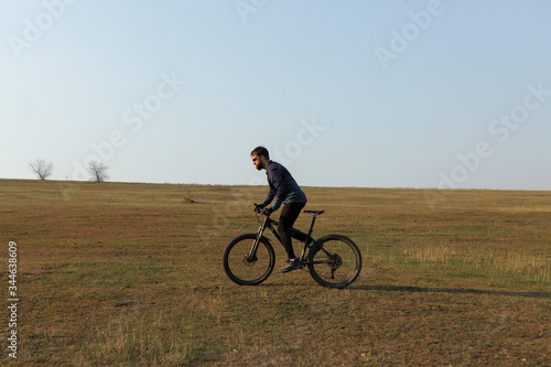 Cyclist in shorts and jersey on a modern carbon hardtail bike with an air suspension fork standing on a cliff against the background of fresh green spring forest