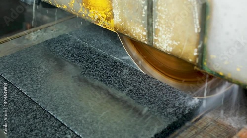 large industrial stone cutter cuts ground gray granite on tiles in water jets. Reflecting a saw in wet granite close up top angle