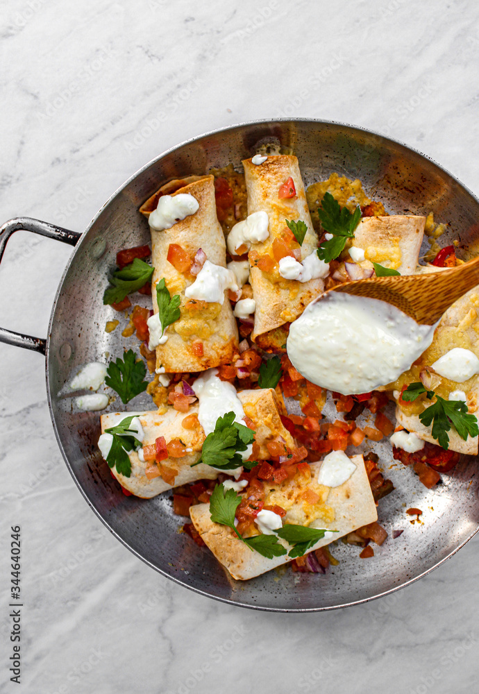 Mexican enchiladas topped with cheese, yoghurt sauce and coriander garnish. Vegetarian enchiladas made with lentils and red peppers. Mexican fast food. Mexican enchiladas topped with cheese, yoghurt sauce and coriander garnish. Vegetarian enchiladas made with lentils and red peppers. Mexican fast food.