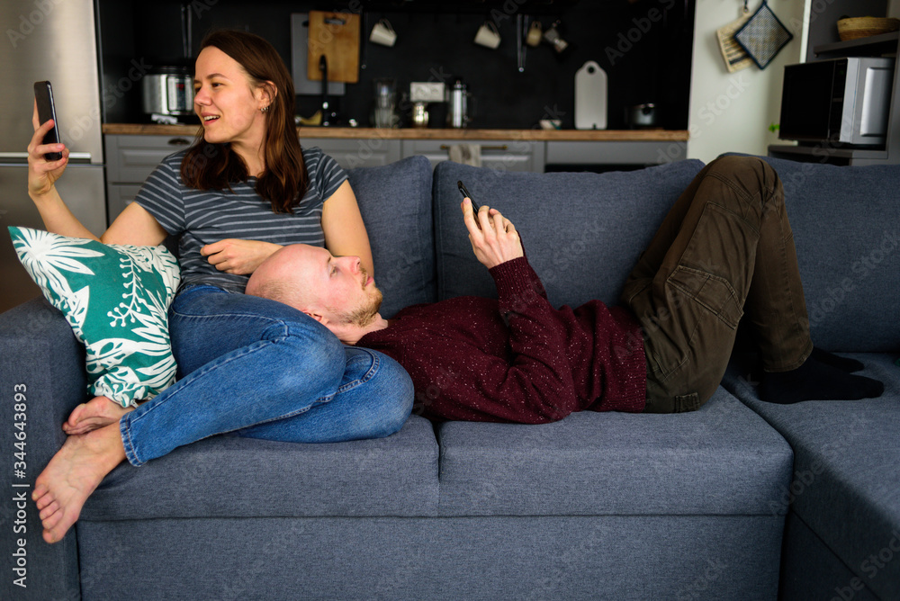 Couple using phones sitting on couch in kitchen Couple using phones sitting on couch in kitchen