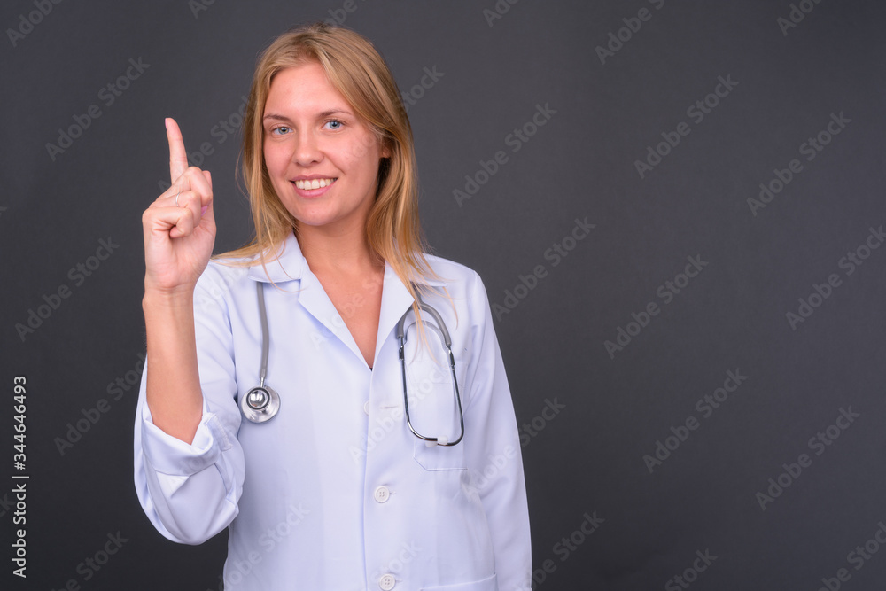 Portrait of happy young blond woman doctor pointing up Portrait of happy young blond woman doctor pointing up