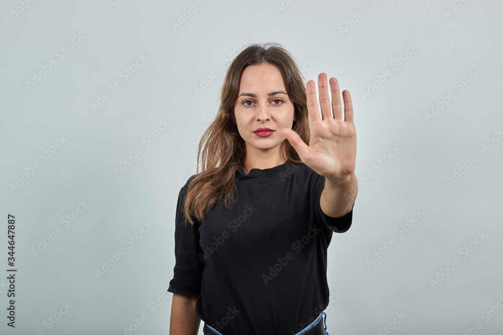 Cute Young Brunette Woman In Black T-Shirt, Blue Jeans With Belt On Gray Background, Dissenting Girl Against, Shows Protest, Opposition, Gesturing With Her Hand, Shows Palms As A Stop Sign Cute Young Brunette Woman In Black T-Shirt, Blue Jeans With Belt On Gray Background, Dissenting Girl Against, Shows Protest, Opposition, Gesturing With Her Hand, Shows Palms As A Stop Sign
