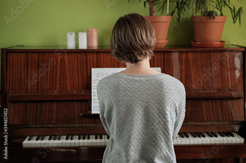 Back view at young woman playing acoustic piano at home. Home islolation.