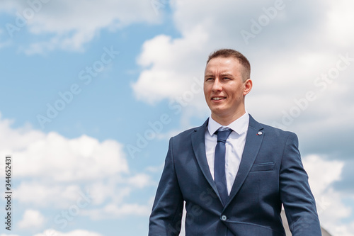 Lifestyle portrait of happy groom outdoor at nature with sky and clouds on background. Cheerful fiance with smiling face in blue jakcet photo