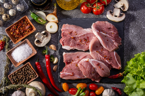 Pork steaks, fresh vegetables, close-up spices on a textured background look from above, culinary background