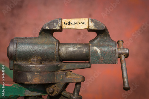 Vice grip tool squeezing a plank with the word tribulation photo