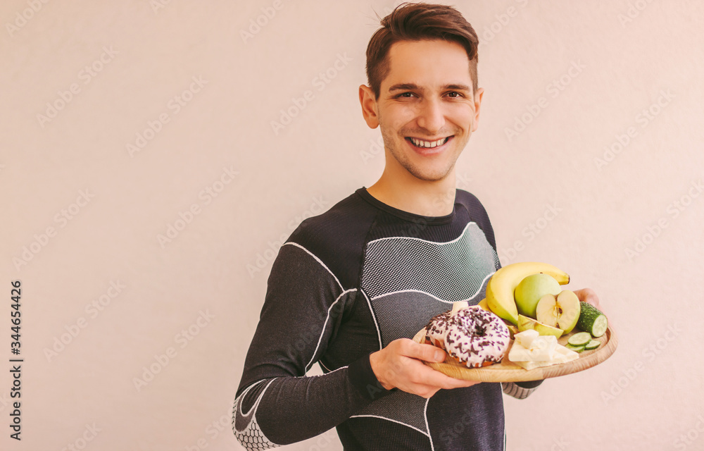 Φωτογραφία Young sports man deciding what to eat: healthy fruits or sugar junk unhealthy snacks