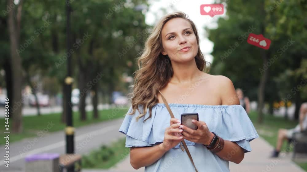 Female enjoys likes in social networks. Young happy woman is walking on the street holding a smartphone in her hands. Female enjoys likes in social networks. Young happy woman is walking on the street holding a smartphone in her hands.