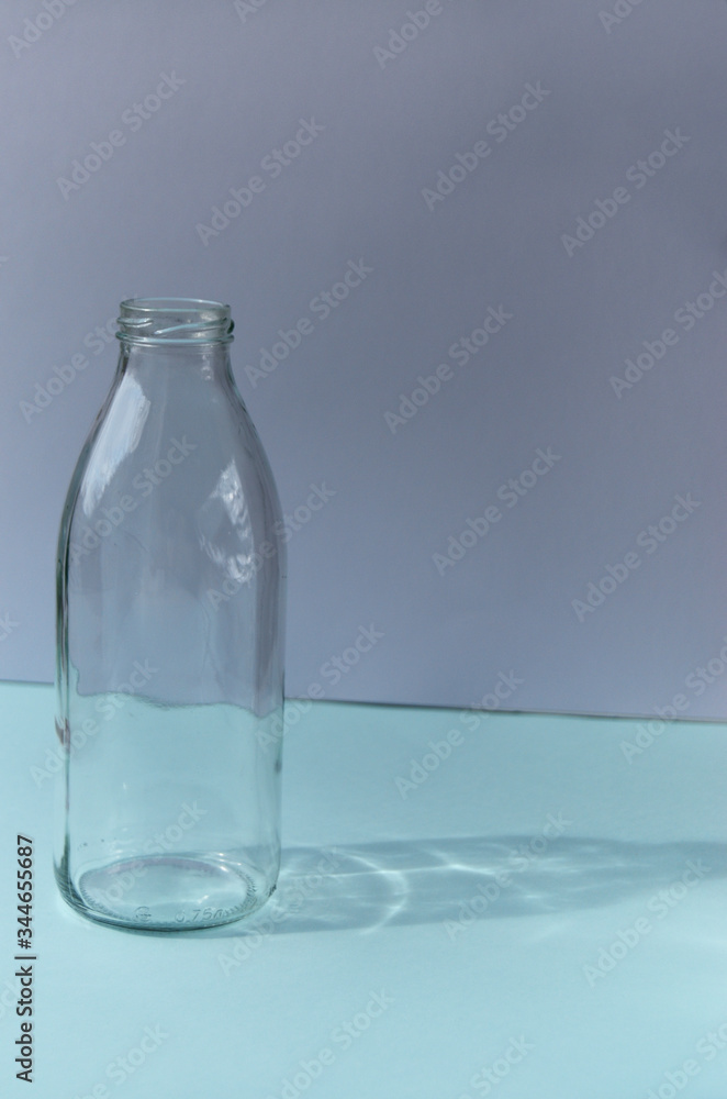 Glass bottle stands on a blue table against the background of a white wall shadow from the bottle sunny Glass bottle stands on a blue table against the background of a white wall shadow from the bottle sunny