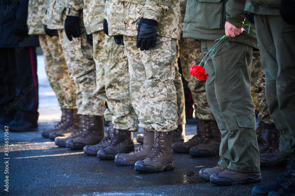 The military stand in a row and one of them holds flowers in his hands
