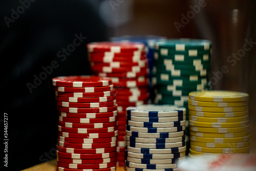 Close up of poker chips in a shallow focus on a wooden table. The gambling chips are green, yellow, blue, white, and red. 