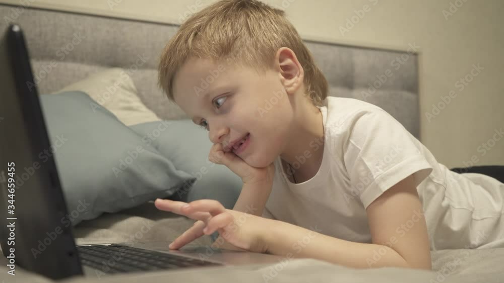 Young boy looking on laptop at home lying on bed. Teenage child using computer . Teenager is typing on laptop keyboard at afternoon . Real time. 4k footage. Young boy looking on laptop at home lying on bed. Teenage child using computer . Teenager is typing on laptop keyboard at afternoon . Real time. 4k footage.