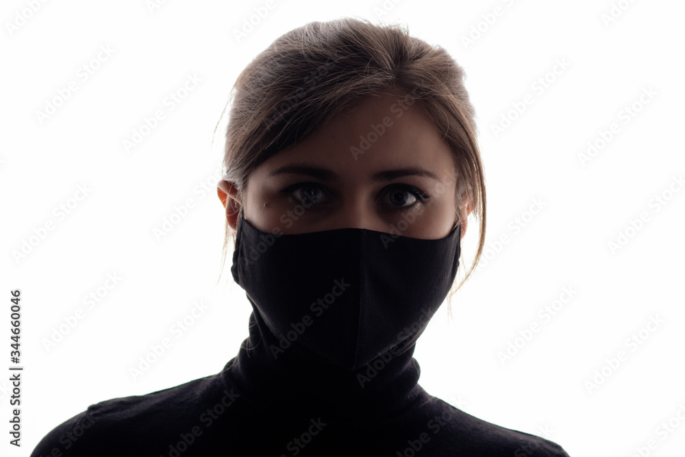 silhouette portrait of young woman in protective black mask covering face on studio background, girl looking like spy agent, concept security