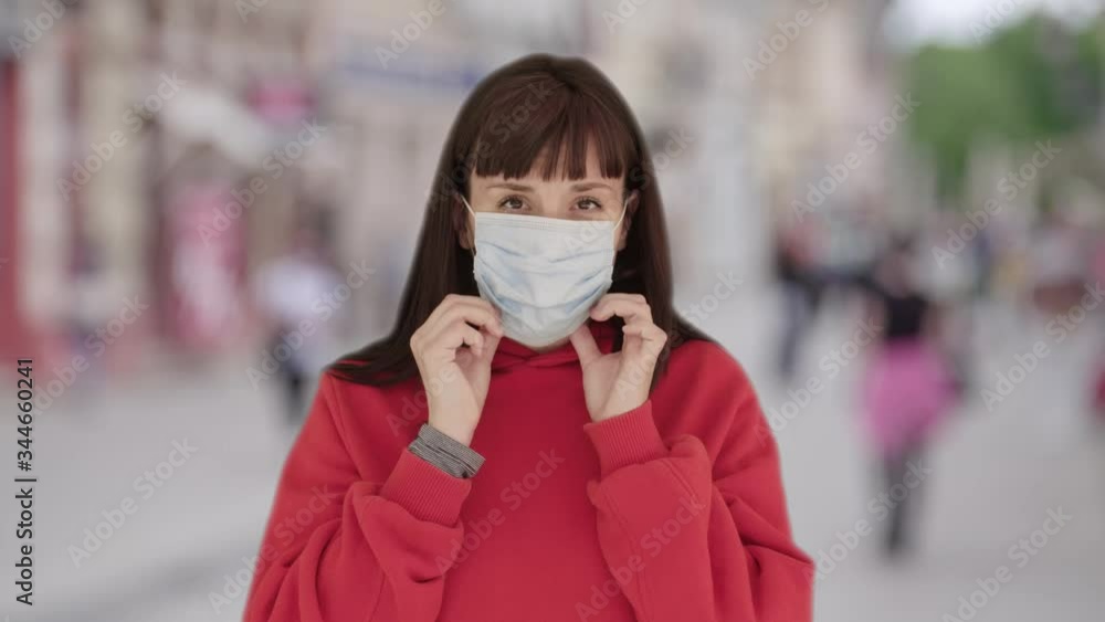 Young woman putting on medical mask crowded street time lapse background covid 19 pandemic crisis Young woman putting on medical mask crowded street time lapse background covid 19 pandemic crisis