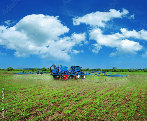 new blue tractor in field work with trailed sprayer, winter crop fertilizers,...