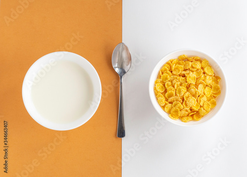 Flat lay with cornflakes and milk in white bowls and metal spoon on beige double background, top view. Concept of healthy breakfast