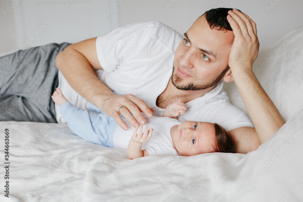 Happy Caucasian father lying with newborn baby in bedroom at home. Man parent holding child daughter son. Authentic lifestyle candid moments. Proud young dad. Family fathers day. Happy Caucasian father lying with newborn baby in bedroom at home. Man parent holding child daughter son. Authentic lifestyle candid moments. Proud young dad. Family fathers day.