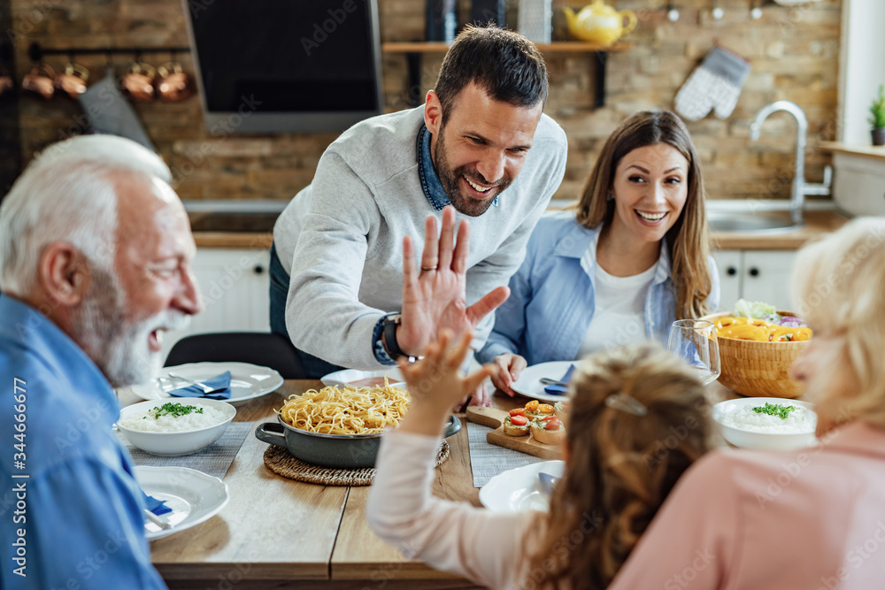 Happy father and daughter giving high-five during a family lunch in dining room. Happy father and daughter giving high-five during a family lunch in dining room.