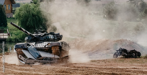 The tank rushes into battle and crushes a passenger car. Glass shatters in different directions and there is a lot of dust around. A show of military equipment. Tank operation.