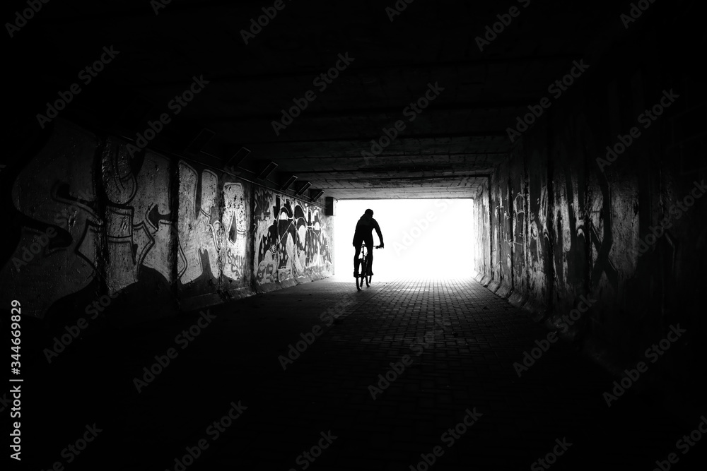 Light at End of Tunnel and Silhouette of Man Driving in Tunnel on bike