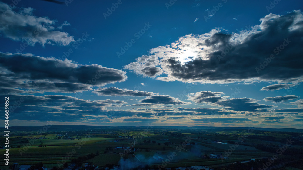 Blue sky and multiple clouds background showing a horizon and a hidden sun