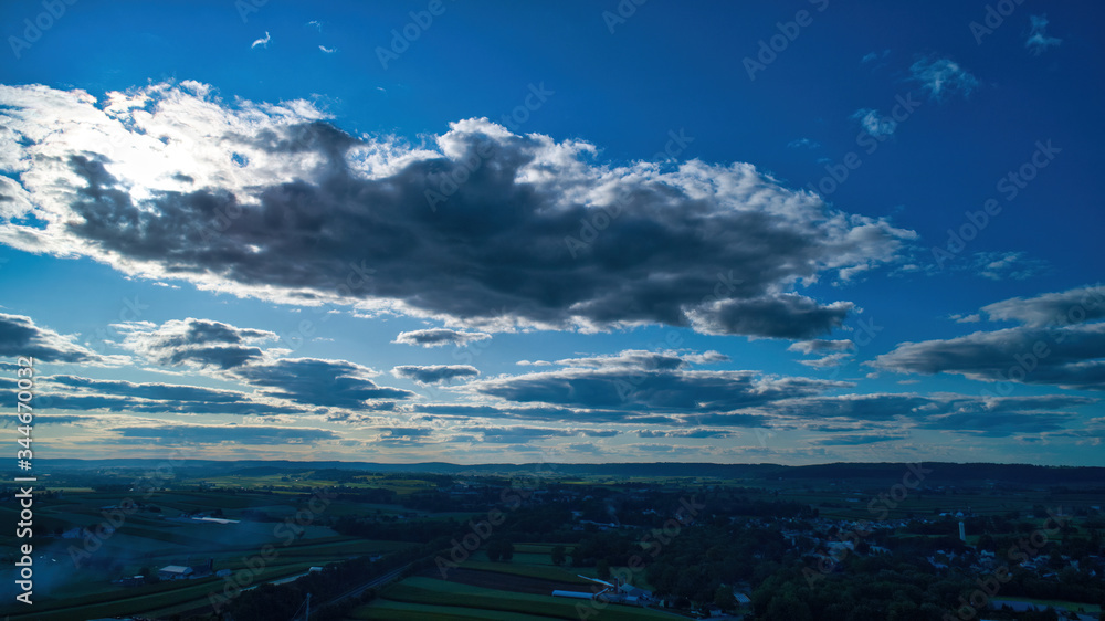 Blue sky and multiple clouds background showing a horizon and a hidden sun