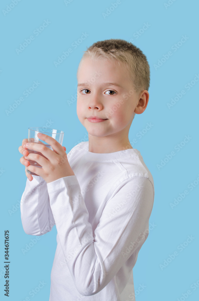 Child holds glass of water in his hands. Blond little boy with water glass, looking at the camera. Child holds glass of water in his hands. Blond little boy with water glass, looking at the camera.