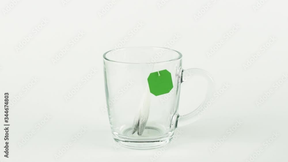 black tea bag with green label is placed in glass transparent mug and filled with boiling water isolated on white background slow motion black tea bag with green label is placed in glass transparent mug and filled with boiling water isolated on white background slow motion
