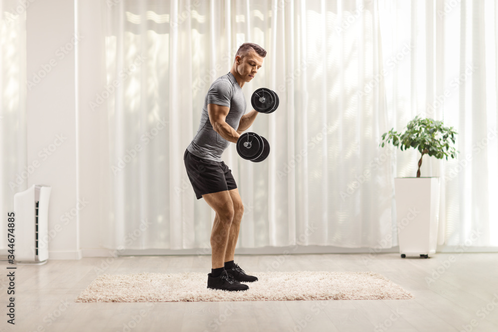 Fototapeta premium Young fit man lifting dumbbells at home
