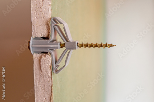 Grey plastic butterfly-type dowel fixed in a pre-drilled hole in a sheet of moisture-resistant drywall, split view. Sheet is cut at installation site, showing the gypsum fiber and connection details.