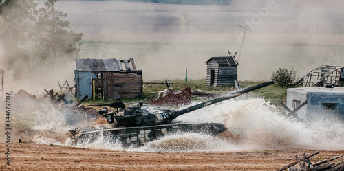 The tank breaks into battle and passes through a huge puddle, there are a lot of splashes of water around. A show of military equipment. Tank operation.