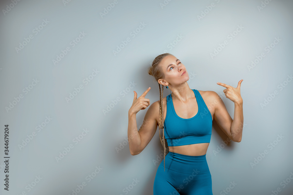 Cheerful, smiling gymnastics girl shows with her hands on a text place, copy space, beautiful body on a gray floor wall background in a yoga studio class.