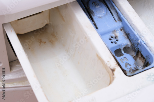 Dirty moldy washing machine detergent and fabric conditioner dispenser drawer compartment close up. Mold, rust and limescale in washing machine tray. Home appliances periodic maintenance concept
