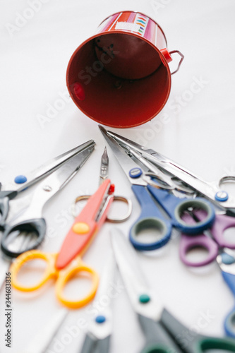 Many multi-colored stationery scissors heading towards the red bucket