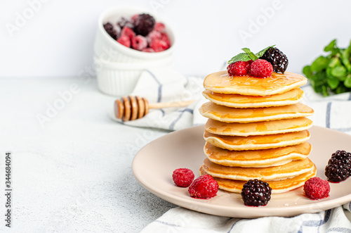 Homemade classic American pancakes with fresh raspberries, blackberries, honey and mint leaves on a grater, light background.