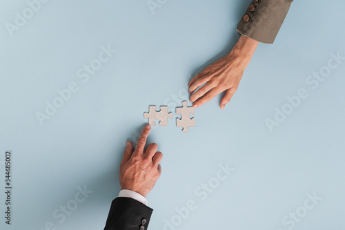 Top view of hands of businesswoman and businessman joining two  matching puzzle pieces