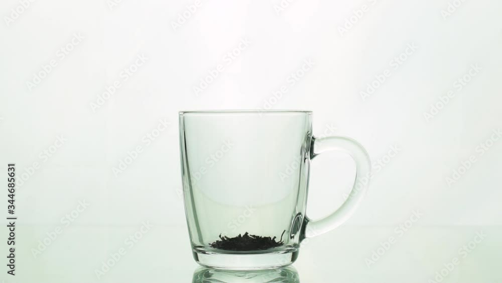 black tea particles pouring into glass transparent mug and adding boiling water to brew tea isolated on white background slow motion black tea particles pouring into glass transparent mug and adding boiling water to brew tea isolated on white background slow motion