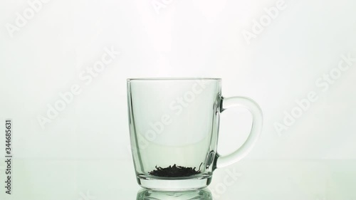 black tea particles pouring into glass transparent mug and adding boiling water to brew tea isolated on white background slow motion