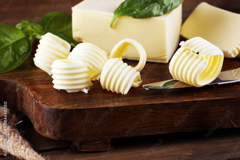 yellow block of fresh butter sliced on wooden cutting board and butter swirls. Slices of margarine or spread, fatty natural dairy product. High-calorie food