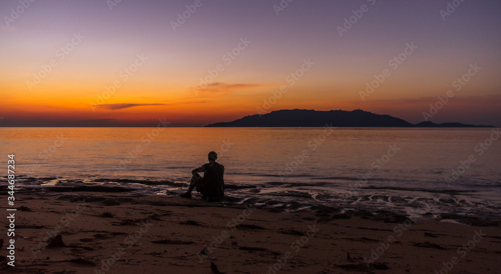 Person sitting and enjoying evening sunset scene with Banda Besar island in distance very bright vibrant sky in Hatta