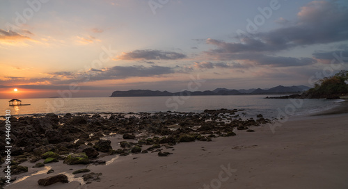 Nice sunset or sunrise moment sunbeam goes through rocky beach scene with hills in distance in Sumbawa, Indonesia