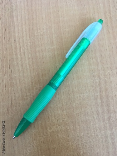 Zielony plastikowy dlugopis lezy na rązowym biurku