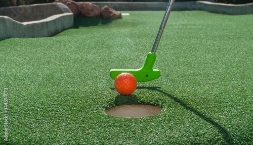Miniature golf putter tapping an orange ball into hole