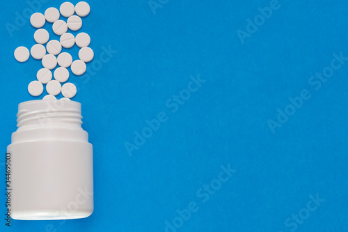 White tablets are dispersed from a bottle on a blue background