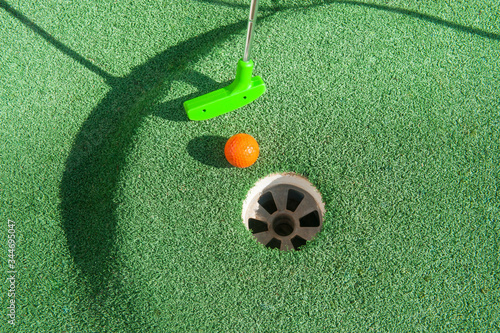 Green mini golf club putts an orange ball towards a hole