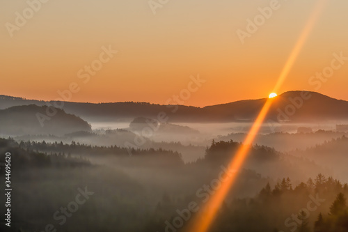 Beautiful landscape of the Bohemian Switzerland at sunrise. Misty morning scenery with sun rising in the background. Bohemian Switzerland, Czech Republic